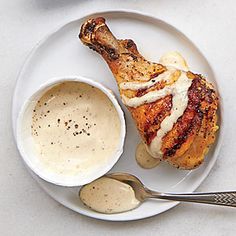 a white plate topped with chicken next to a bowl of sauce and a spoon on top of a table