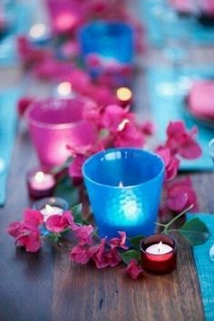 the table is set with pink and blue flowers, candles and napkins on it