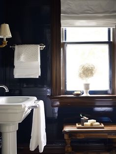 a white sink sitting under a window next to a wooden table with candles on it