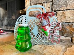 a green christmas tree sitting next to a basket with ornaments on it and a fireplace in the background