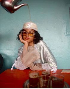 a woman sitting at a table with glasses on her head and a teapot hanging over her head