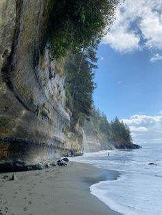 a person walking on the beach next to some cliffs