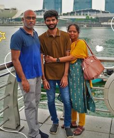 two men and a woman standing next to each other in front of a body of water