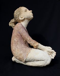 a statue of a woman sitting on the ground with her hands folded in front of her chest