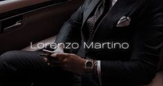 a man in a suit sitting on a car seat looking at his cell phone with the caption lorenzo martinio