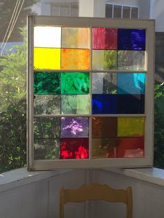 a window that has some colored glass on the side of it and a wooden chair in front of it