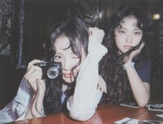 two young women sitting at a table taking pictures