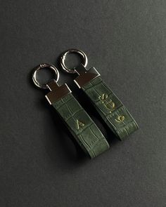 two green leather keychains with metal rings on them sitting on a black surface