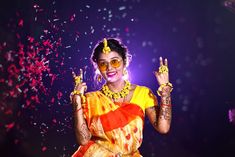 a woman in yellow and red sari holding up two fingers with confetti on it