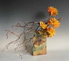 a vase filled with yellow flowers on top of a white table next to a tree branch