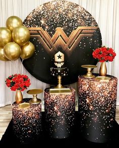 a table topped with vases filled with red flowers and gold foil balloons in front of a black backdrop