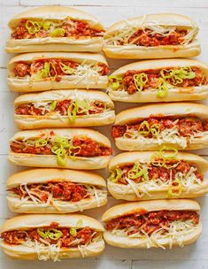 many hot dogs are lined up on a white surface with shredded cheese and meat toppings