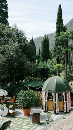 an outdoor patio with tables and umbrellas in the shade, surrounded by greenery