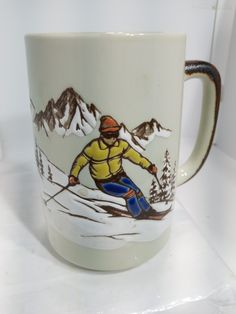 a coffee cup with a skier painted on the side and mountains in the back ground