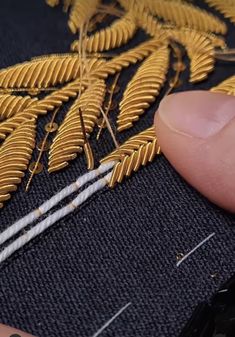 someone is stitching gold leaves on a black piece of fabric with white pins and thread