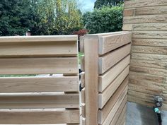 a close up of a wooden fence near a brick wall and grass area with trees in the background