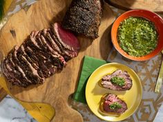 some meat and sauces are sitting on a wooden cutting board next to two bowls