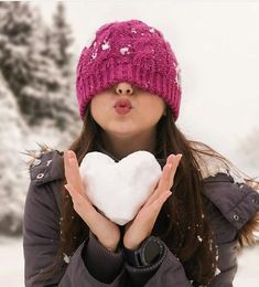 a woman holding a heart shaped snowball in her hands while wearing a pink hat