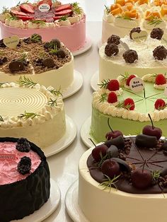 several cakes are arranged on white plates and one is decorated with cherries, strawberries, and chocolate