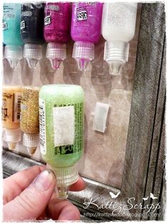 a person is holding a tube of soap in front of a shelf with different colored bottles