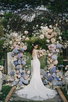 a woman standing in front of a floral arch with blue and pink flowers on it