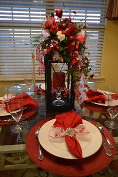 the table is set with red napkins, silverware and flowers in a vase