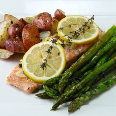 asparagus, potatoes and salmon on a white plate with lemon wedges next to them