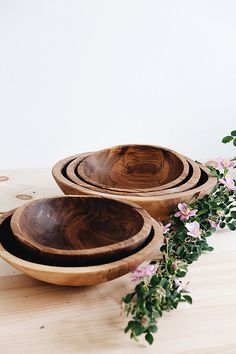 three wooden bowls sitting on top of a wooden table next to flowers and greenery