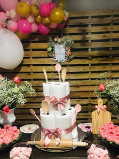 a table topped with lots of pink and white cake next to balloons in the air