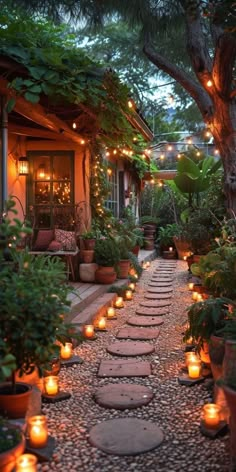 an outdoor walkway with lit candles and potted plants on the side, surrounded by greenery