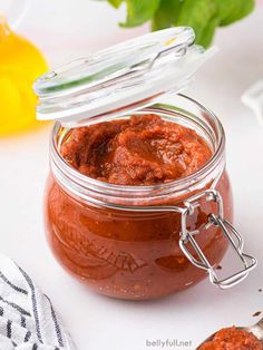 a jar filled with red sauce sitting on top of a white table next to lemons