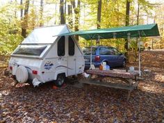 a camper parked in the woods next to a picnic table with a tent on it