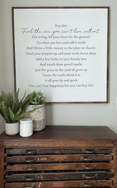 a wooden dresser with two potted plants sitting on top of it next to a framed poem