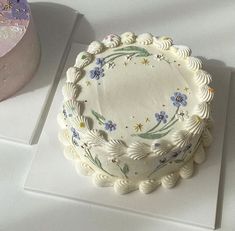 a white cake sitting on top of a table next to a frosted cupcake