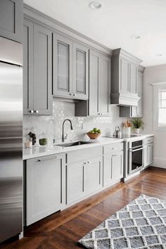 a kitchen with gray cabinets and white counter tops, hardwood floors, and a rug