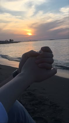 two people holding each other's hands on the beach as the sun goes down