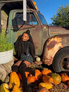 a woman sitting on the ground in front of an old truck surrounded by pumpkins