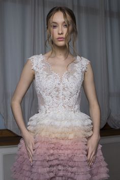 a woman standing in front of a window wearing a pink and white dress with ruffled layers