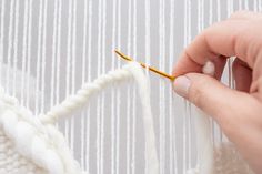 someone is knitting something on a piece of white yarn with a yellow crochet hook