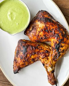 two grilled chicken legs on a white plate with a green dip