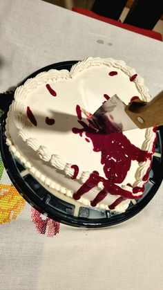 someone is cutting into a heart shaped cake with white frosting and red sprinkles