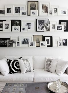 a living room filled with white furniture and lots of pictures on the wall above it