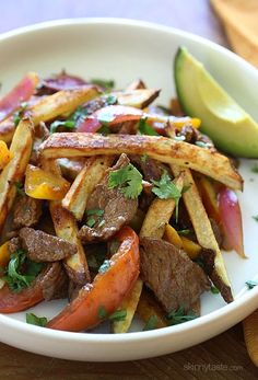 a white plate topped with steak and fries next to a sliced avocado on top of a wooden cutting board