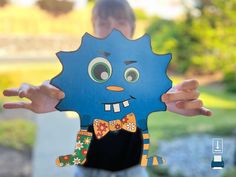 a person holding up a paper cut out of a blue monster with big eyes and a bow tie