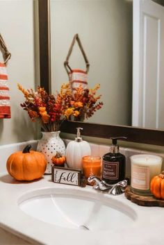 a white sink sitting under a mirror next to a candle and some pumpkins on top of it