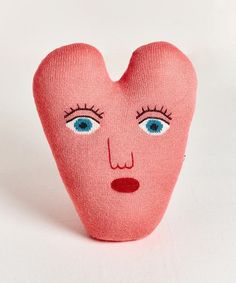 a pink heart shaped pillow with blue eyes and eyelashes on it's face, against a white background