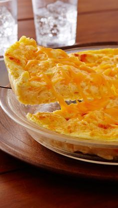 an omelet with cheese is on a plate next to two glasses and silverware