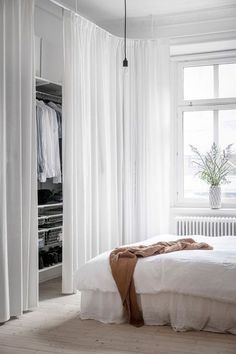 a bedroom with white curtains, a bed and a plant on the window sill