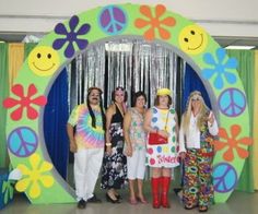 group of women standing in front of a peace sign backdrop with flowers and smiley faces on it