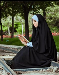 a woman in a nun outfit reading a book on the ground with trees behind her